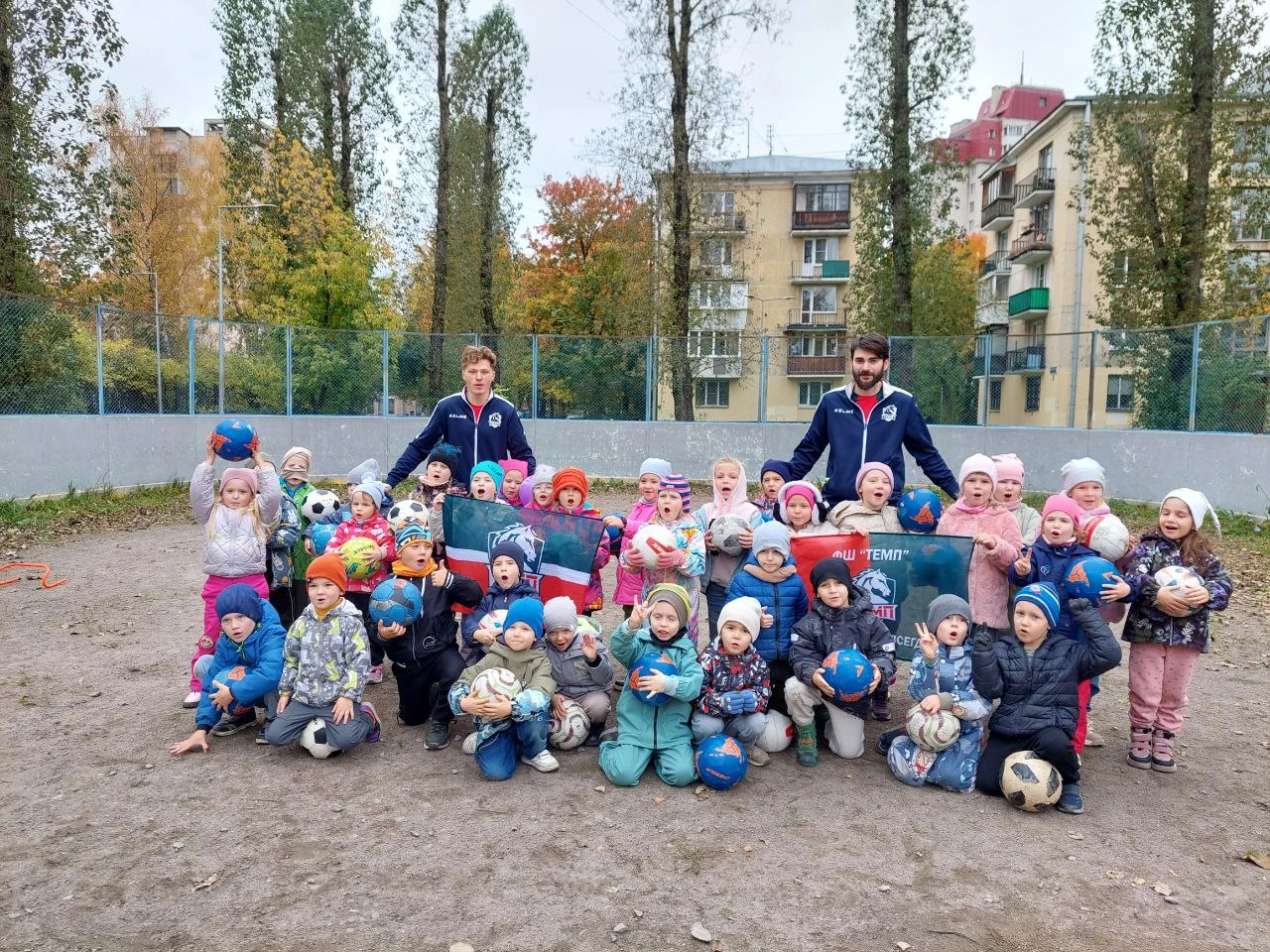 Дети с мячами и спортивные наставники на площадке
